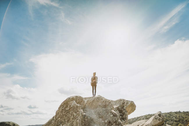 Молода жінка стоїть на скелі на сонячному небі — стокове фото