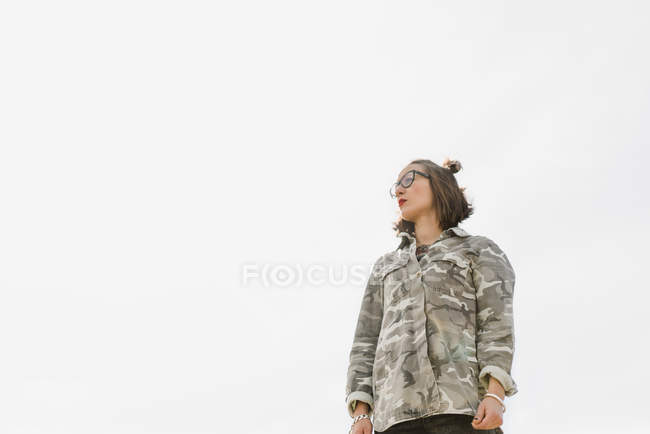 Thoughtful woman in glasses standing against sky and looking away. — Stock Photo