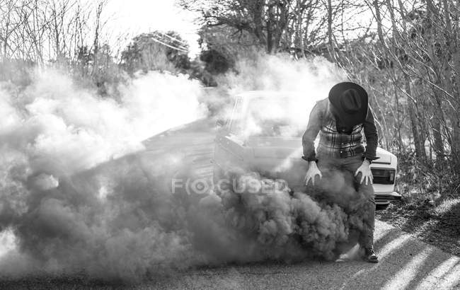 Man coughing by broken vintage car emitting smoke at country road — Stock Photo