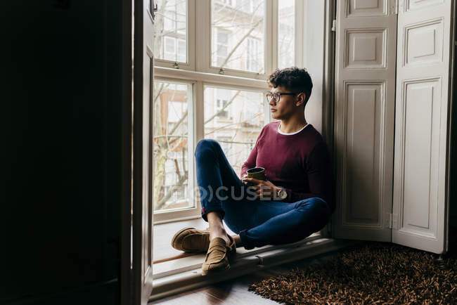 Man with cup sitting on window sill — Stock Photo