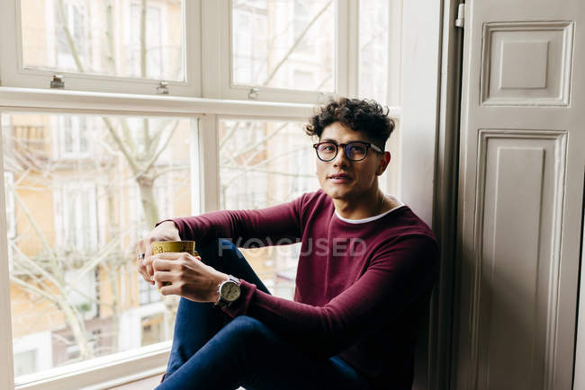 Man with cup sitting on window sill and smiling — Stock Photo