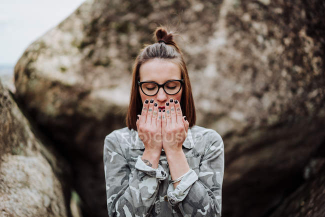 Mulher em óculos cobrindo lábios com palmas contra pedras — Fotografia de Stock