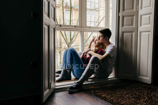 Young couple sitting on window sill and hugging — Stock Photo