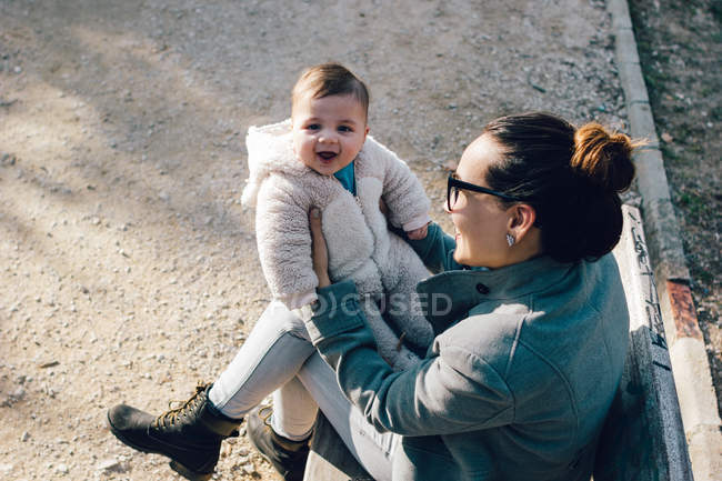 Cute toddler on mother hands looking at camera at park — Stock Photo