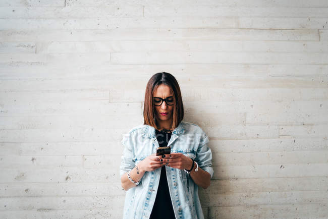Bruna donna che naviga smartphone al muro di cemento — Foto stock