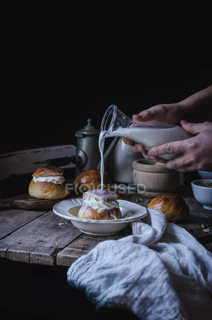 Crop hands of serving bun and pouring it over with fresh milk. — Stock Photo