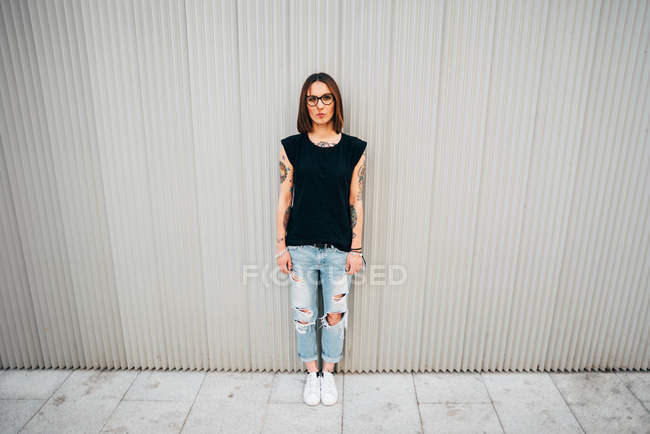 Stylische junge Frau steht an Metallwand und blickt in die Kamera — Stockfoto
