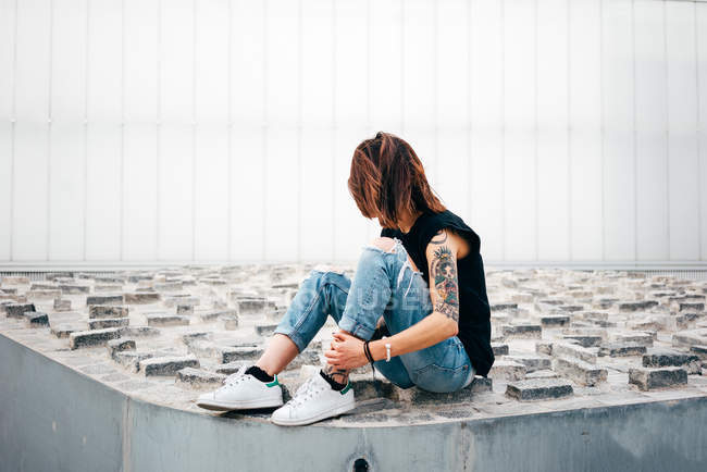 Side view of tattooed woman sitting on old relief pavement on street. — Stock Photo