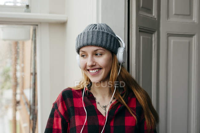 Cheerful blonde woman in knitted hat wearing headphones — Stock Photo