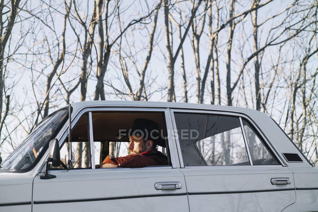 Бородатий чоловік у капелюсі керує старовинною білою машиною в природі . — стокове фото