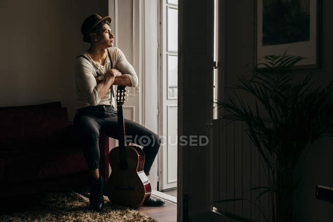 Задумчивый человек в винтажной одежде с гитарой у окна — стоковое фото