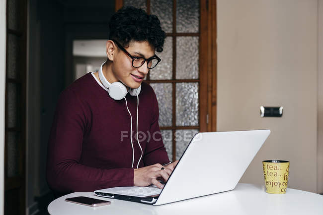 Jeune homme en lunettes tapant sur ordinateur portable à la maison — Photo de stock