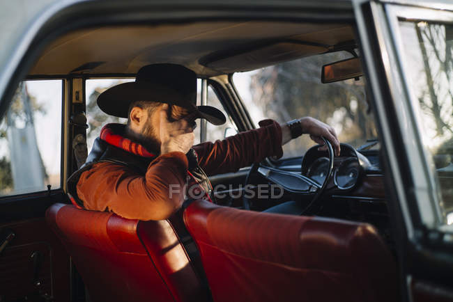 Homem de chapéu sentado no carro no assento do motorista com palma na cara — Fotografia de Stock