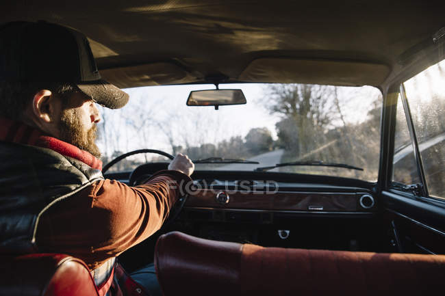 Bearded man in hat driving vintage car in nature. — Stock Photo