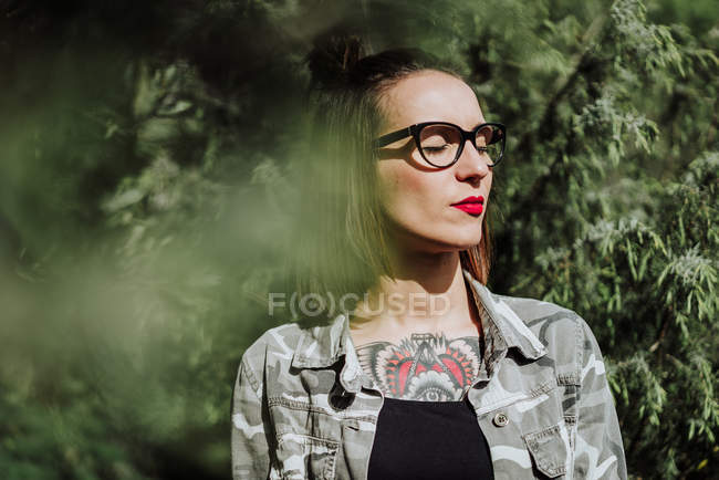 Jovem mulher de óculos de pé com os olhos fechados na natureza . — Fotografia de Stock