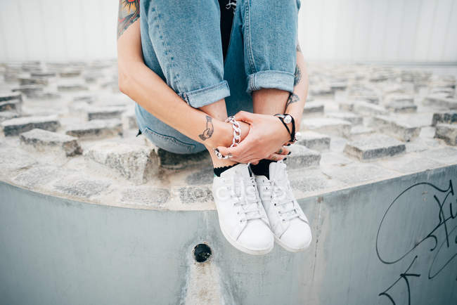 Обрізати татуйовану жінку, сидячи на тротуарі і захоплюючи ноги — стокове фото