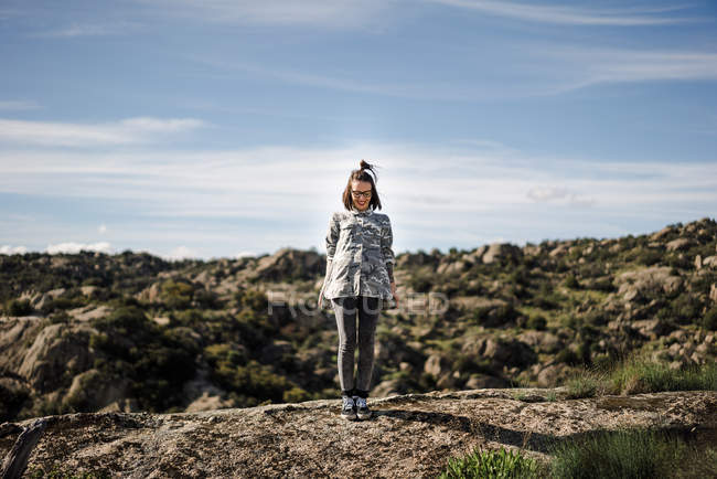 Young woman standing on cliff against rocky landscape and sky — Stock Photo