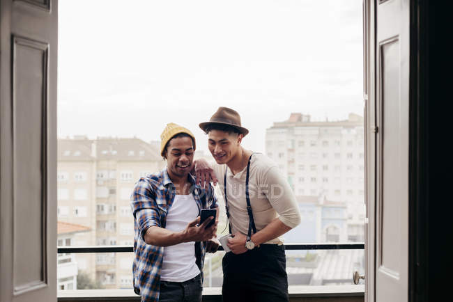 Amigos multiétnicos mirando en el teléfono inteligente en el balcón - foto de stock
