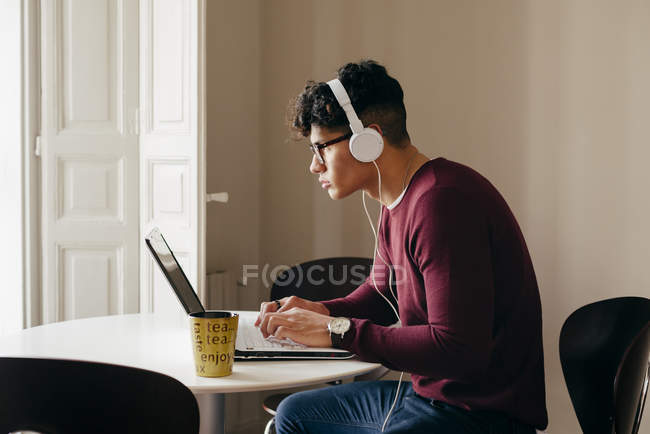 Вид сбоку человека в наушниках, просматривающего ноутбук дома — стоковое фото