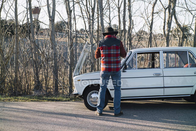 Вид ззаду чоловіка, що відкриває капюшон старовинного автомобіля в природі . — стокове фото