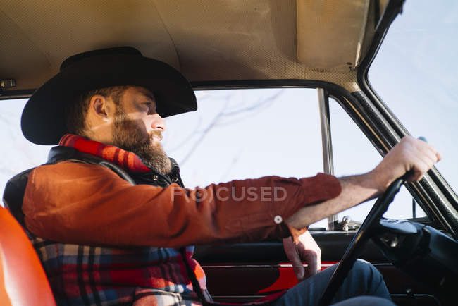 Бородатий чоловік у капелюсі за кермом старовинної машини в сонячний день — стокове фото