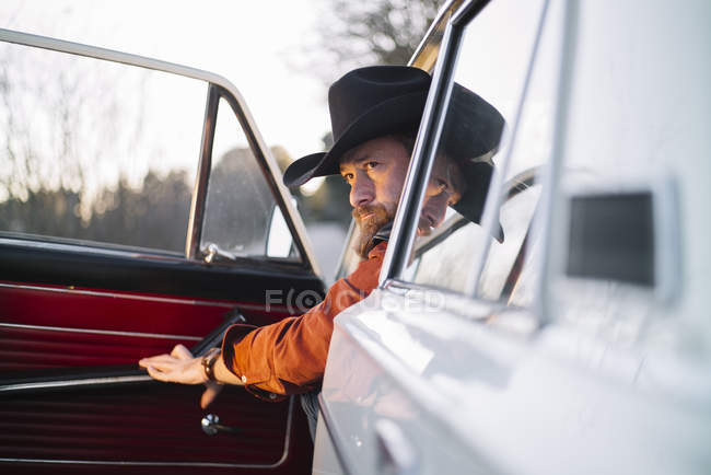 Homem pensativo de chapéu sentado no carro branco vintage e porta de fechamento — Fotografia de Stock