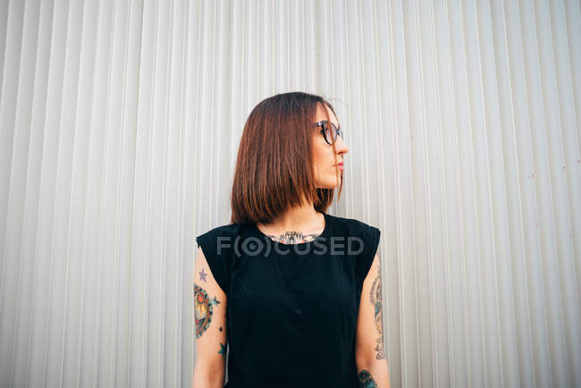 Stylische tätowierte Frau steht an Metallwand und schaut zur Seite — Stockfoto