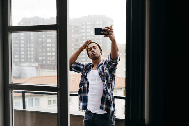 Elegante giovane uomo in piedi sul balcone e prendere selfie . — Foto stock