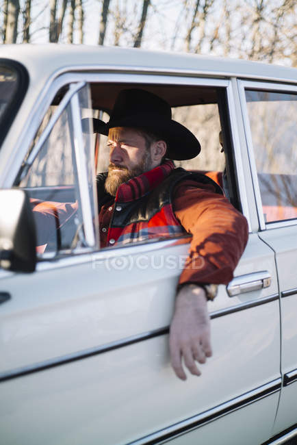 Homme barbu en chapeau conduisant voiture blanche dans la nature . — Photo de stock