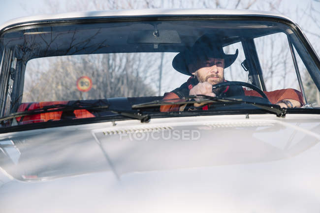 Uomo barbuto in cappello guida auto d'epoca bianca in natura . — Foto stock