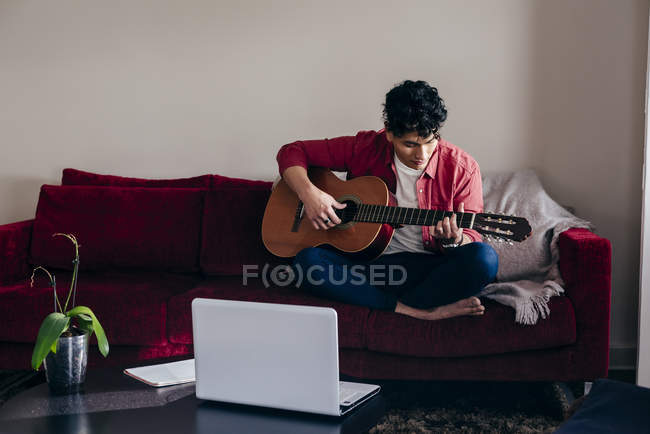 Jovem tocando guitarra no treinador em casa — Fotografia de Stock