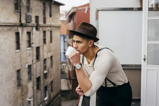 Чоловік в капелюсі п'є каву на балконі — стокове фото