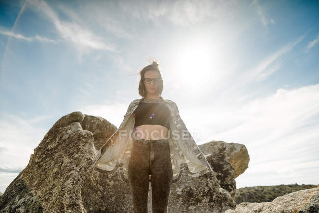 Thoughtful woman in glasses posing by cliffs on sunny day — Stock Photo