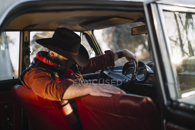 Hombre con sombrero sentado en el asiento del conductor y mirando hacia abajo - foto de stock