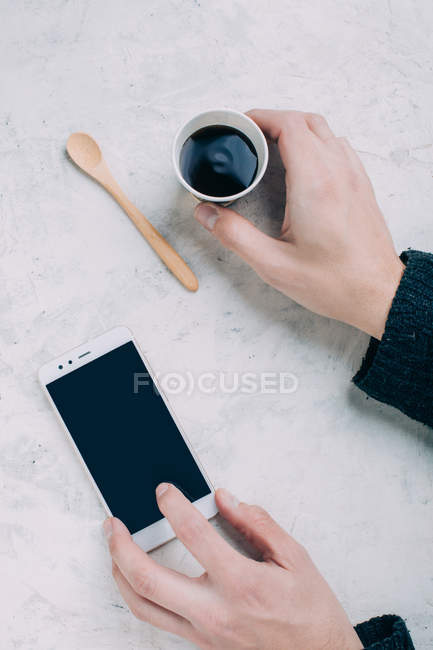 Crop mains masculines tenant café noir dans une tasse jetable et smartphone — Photo de stock