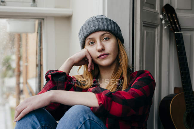 Pensive blonde woman posing at window with cheek on hand — Stock Photo