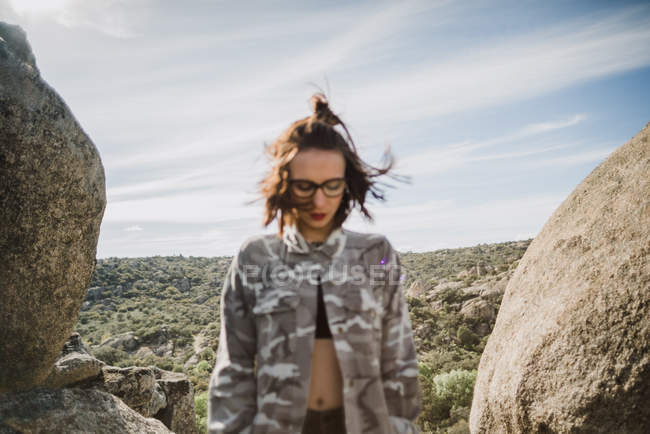 Гарненька молода жінка стоїть серед скелі на тлі сонячного ландшафту — стокове фото