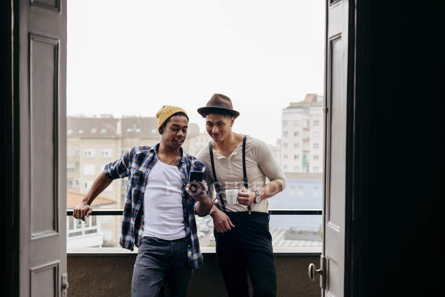 Amigos multiétnicos posando con smartphone en balcón - foto de stock