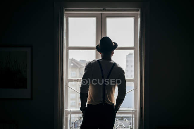 Вид сзади на человека в шляпе, смотрящего в окно — стоковое фото