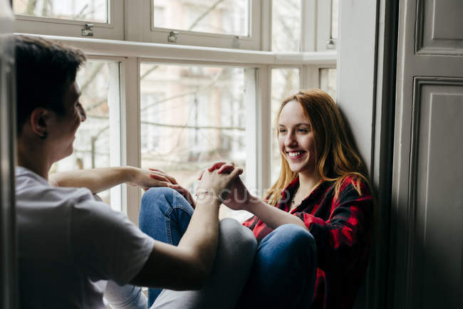 Couple sitting on window sill face to face and holding hands — Stock Photo