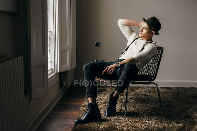 Стильный мужчина в винтажной одежде позирует на стуле у окна — стоковое фото