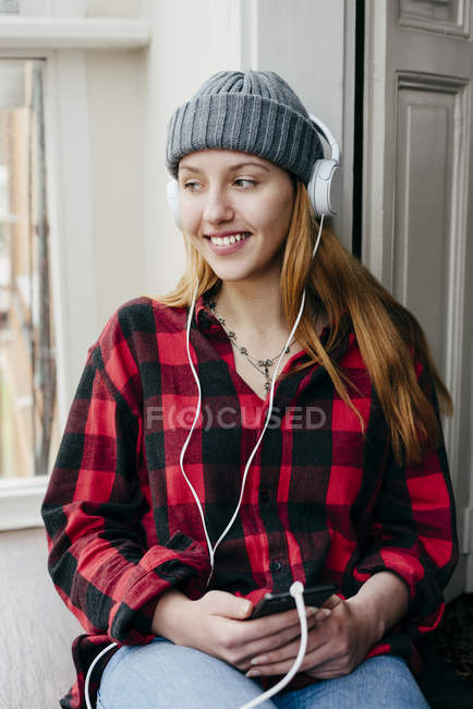 Cheerful blonde woman with smart phone and headphones enjoying music at home — Stock Photo