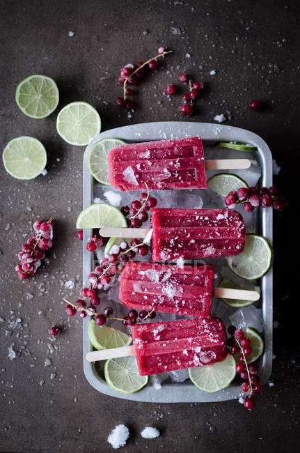 Vue de dessus de la glace rouge sur bâtonnets servie avec des morceaux de lime dans le récipient . — Photo de stock