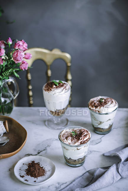 Still life of sweet desserts in glasses on table with bouquet — Stock Photo
