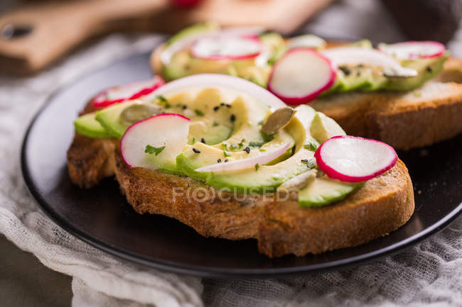Close up view of toasts with avocado and radishes on plate — Stock Photo