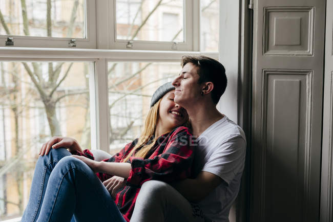 Alegre pareja sentado en ventana alféizar y abrazando sensualmente - foto de stock