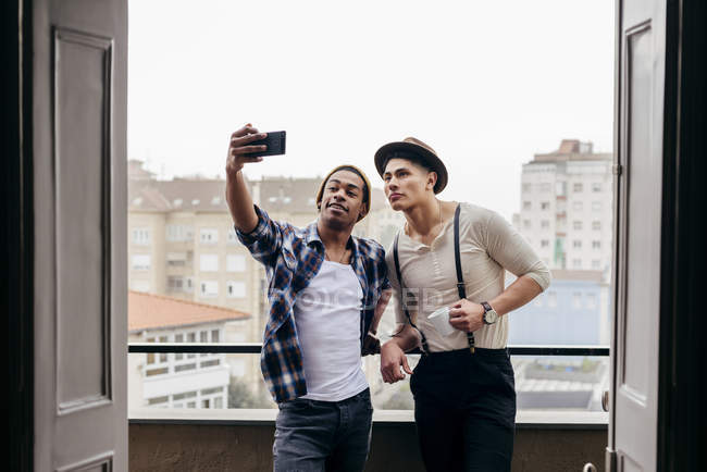 Giovani amici multietnici in piedi insieme e prendere selfie sul balcone a casa . — Foto stock