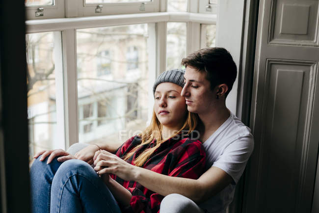 Sereno joven pareja abrazando en ventana alféizar ar casa - foto de stock