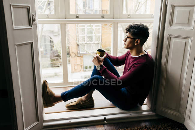 Man with cup sitting on window sill and looking away — Stock Photo