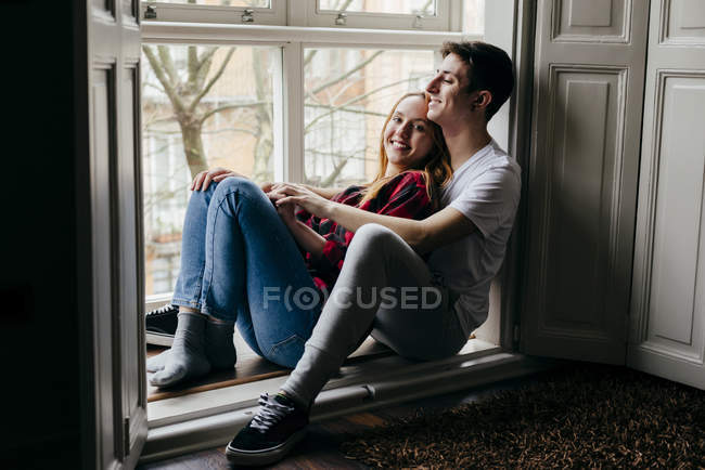 Smiling couple hugging happily on window sill at home — Stock Photo